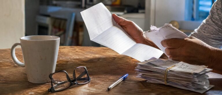 Maos segurando uma carta de indeferimento do INSS sobre a mesa de casa, ao lado de recibos medicos